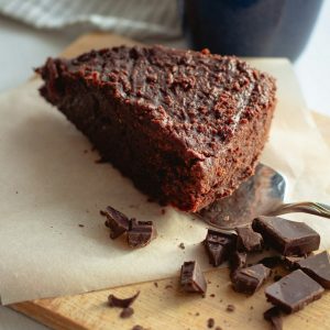 Decadent chocolate cake slice with chocolate chunks on a cutting board.