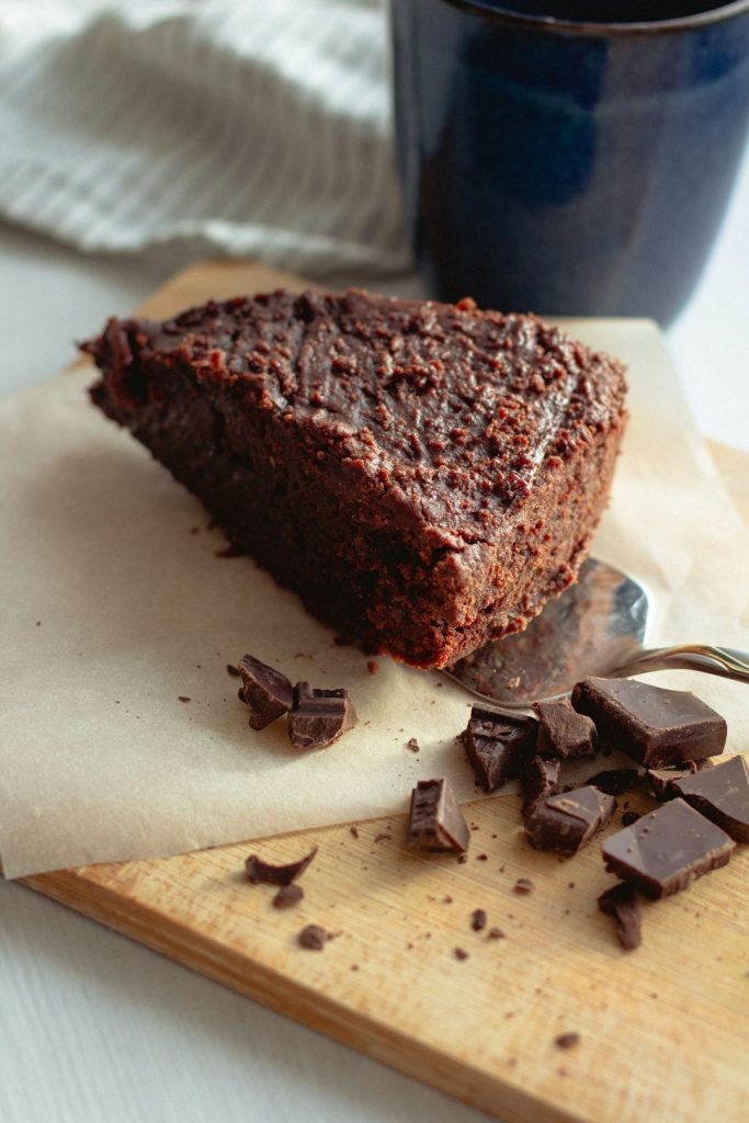 Decadent chocolate cake slice with chocolate chunks on a cutting board.