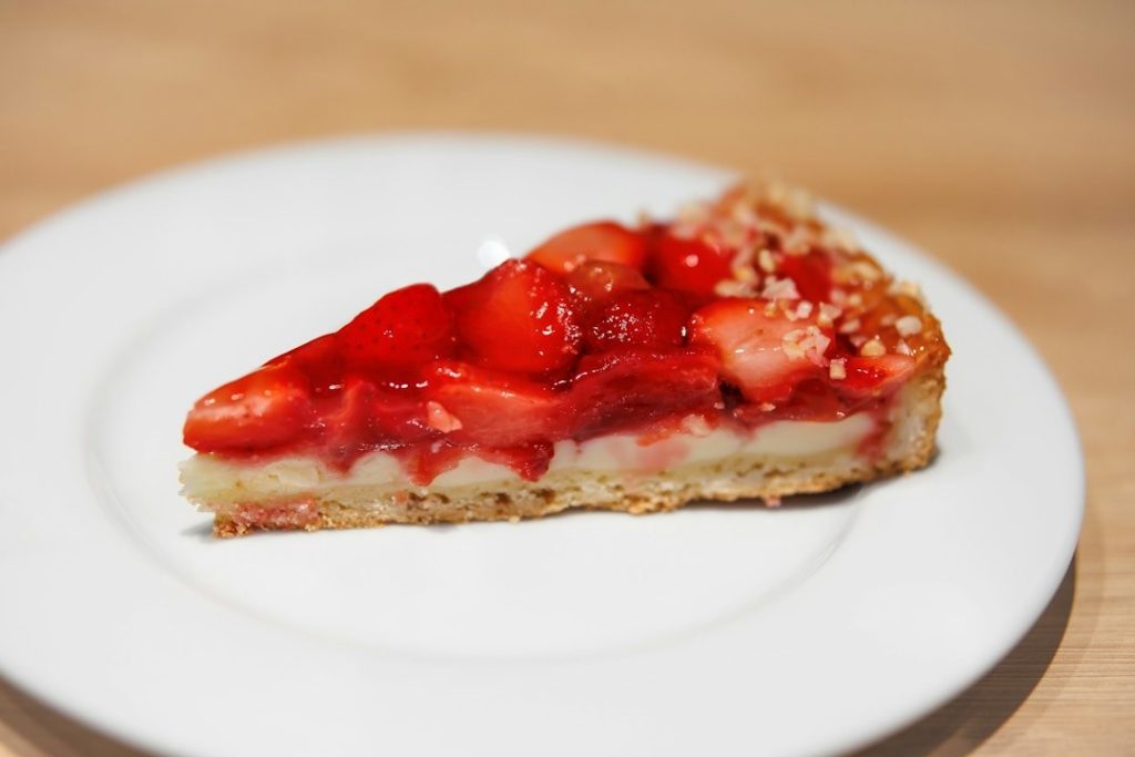 Slice of strawberry tart with fresh strawberries and cream on a plate.