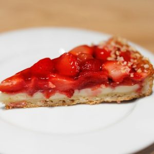 Slice of strawberry tart with fresh strawberries and cream on a plate.